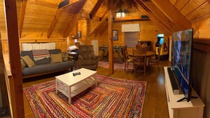 A cozy log cabin interior with a sofa, armchair, coffee table, and a foosball table. - Naked Creek Cabin (Page County)