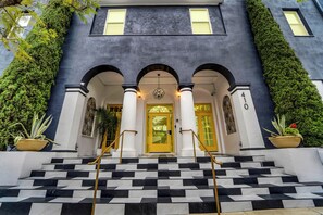 A building with a dark facade, a yellow door, and a staircase with black and white tiles. - The Neon Elm Hotel (San Diego)