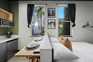 A modern hotel room with a bed, a dining table with a remote control, a microwave, and a small plant. - The Neon Elm Hotel (San Diego)