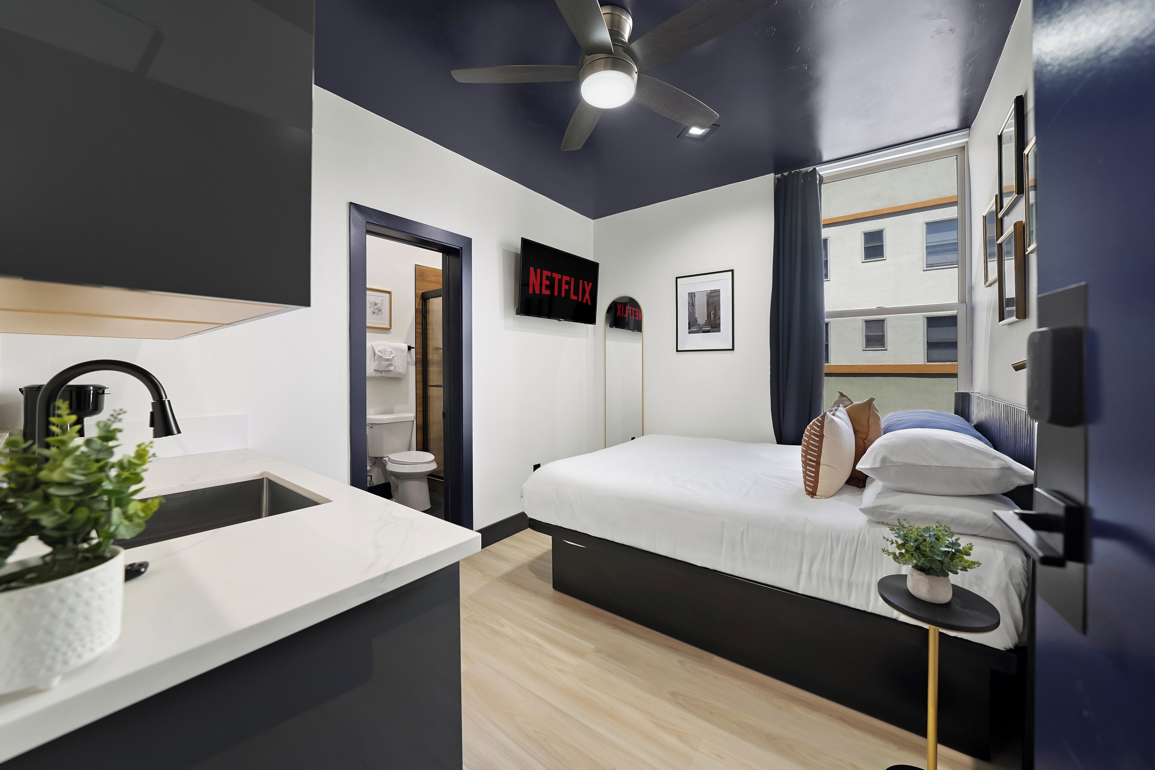 A modern hotel room with a bed, bedside table, and a TV displaying the Netflix logo.