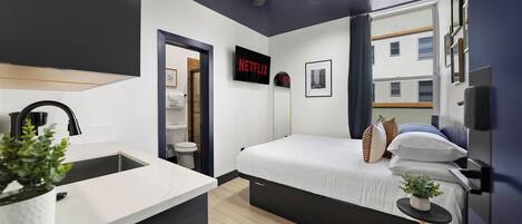 A modern hotel room with a bed, bedside table, and a TV displaying the Netflix logo.