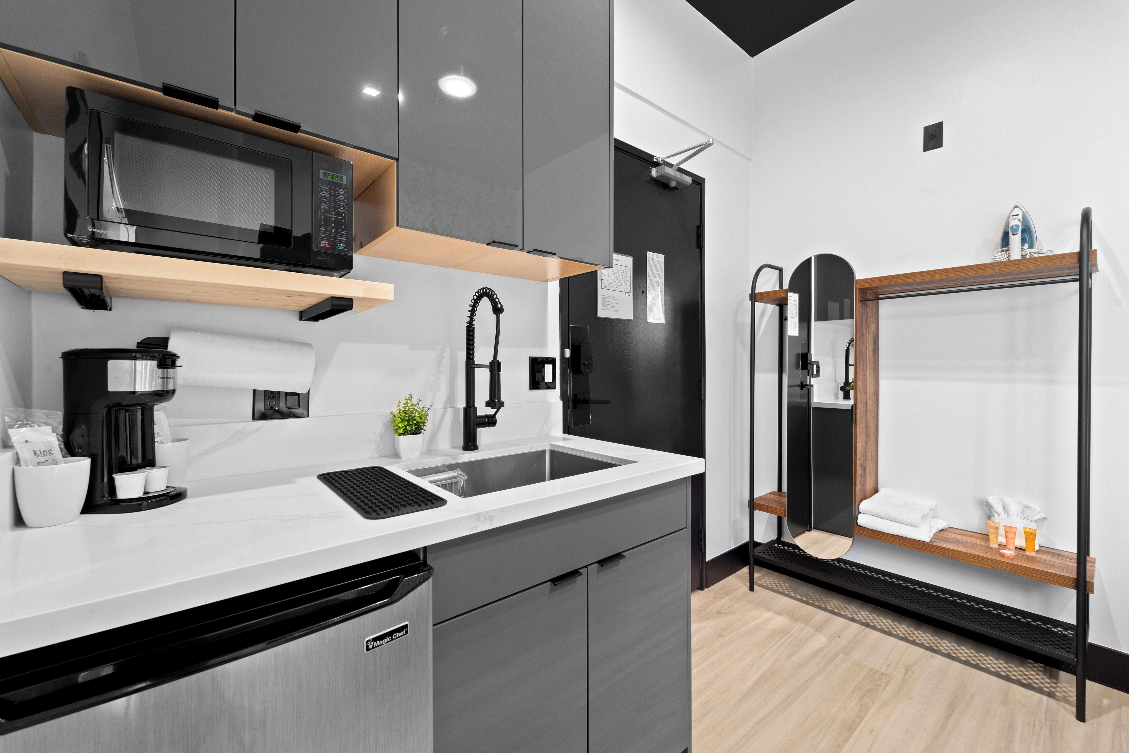 Een moderne keuken met een magnetron, koffieapparaat, spoelbak en een kleine plant.