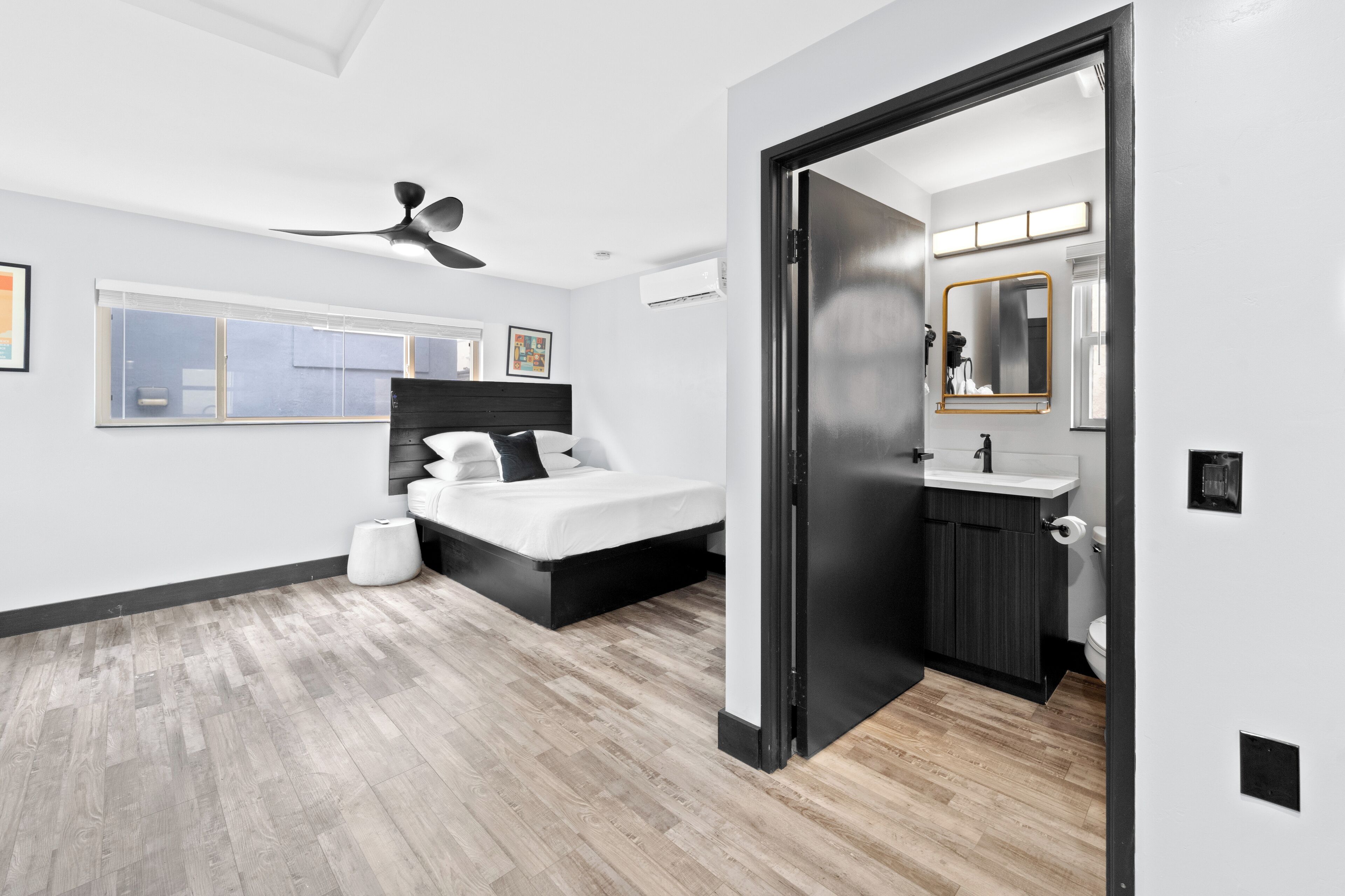 A modern bedroom with a bed, a ceiling fan, and a bathroom with a sink and mirror.