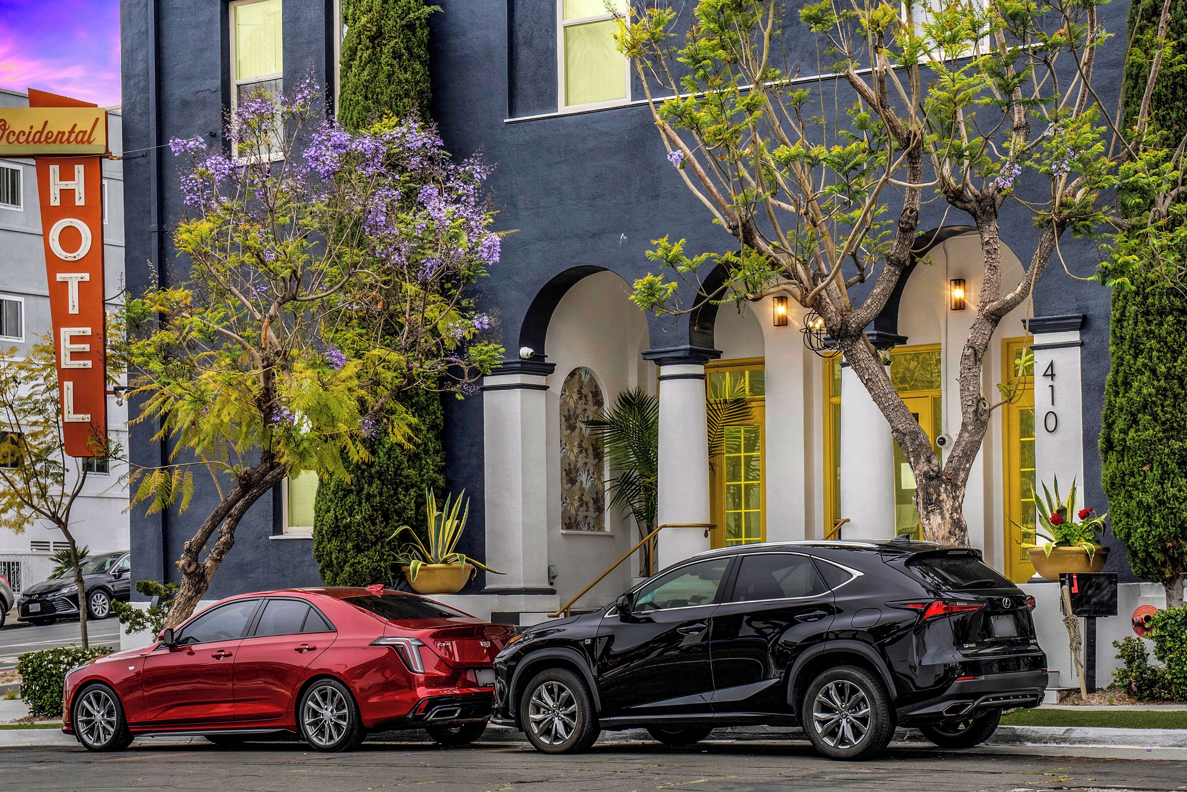 A hotel with a prominent 'HOTEL' sign, a black SUV parked in front, and a red car parked beside it.