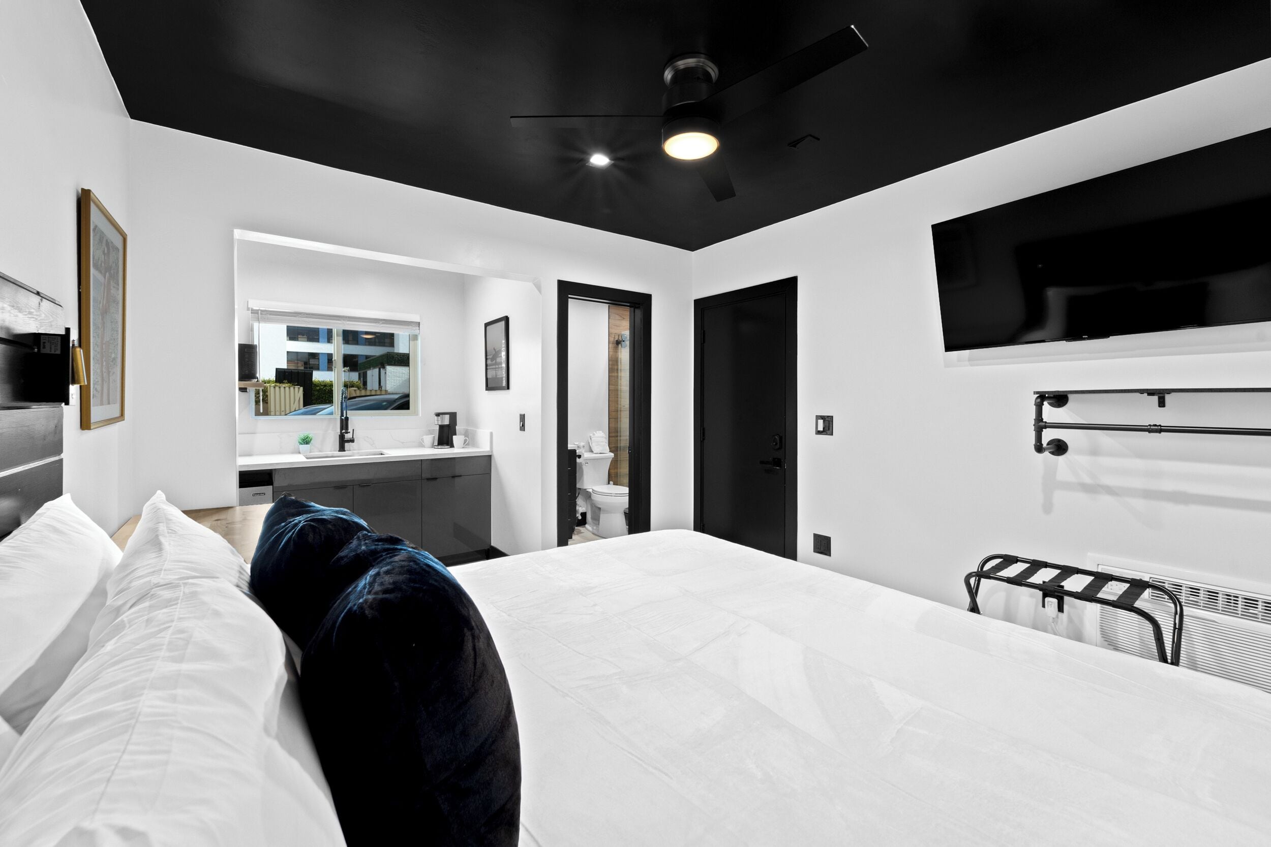 A modern hotel room with a large bed, a ceiling fan, a mounted TV, and a view of the outside.