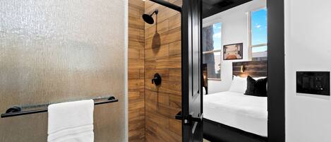 A modern bathroom with a glass shower enclosure, wooden wall tiles, and a white towel hanging on a rack.