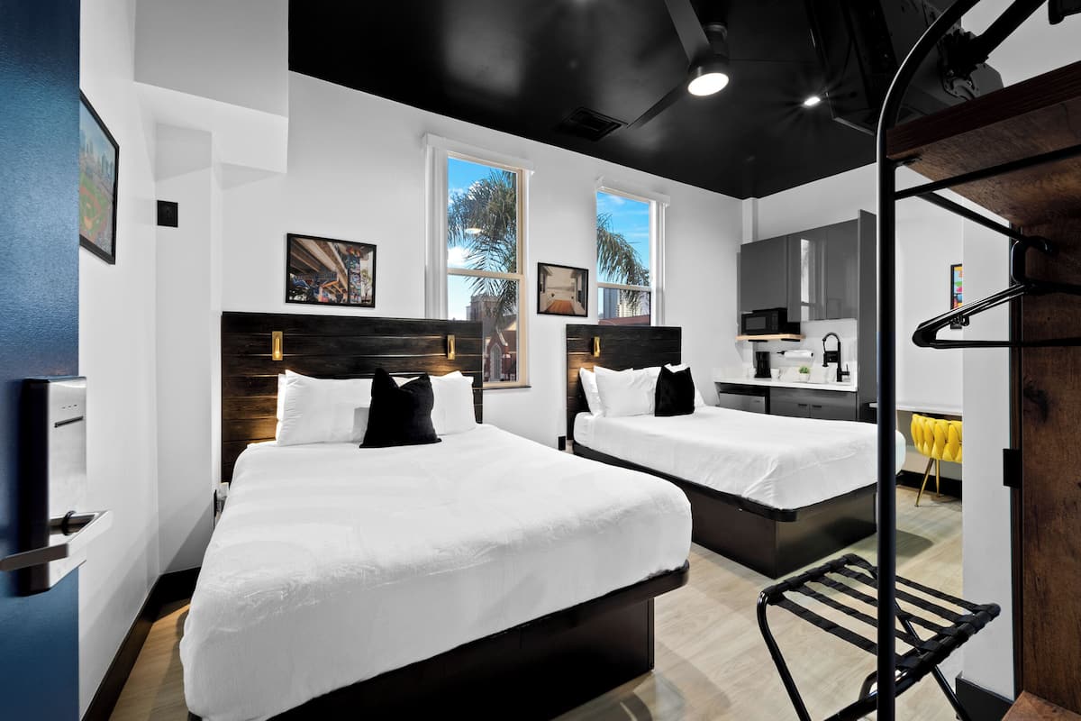 Una habitación de hotel moderna con dos camas, una kitchenette pequeña y ventanas amplias.