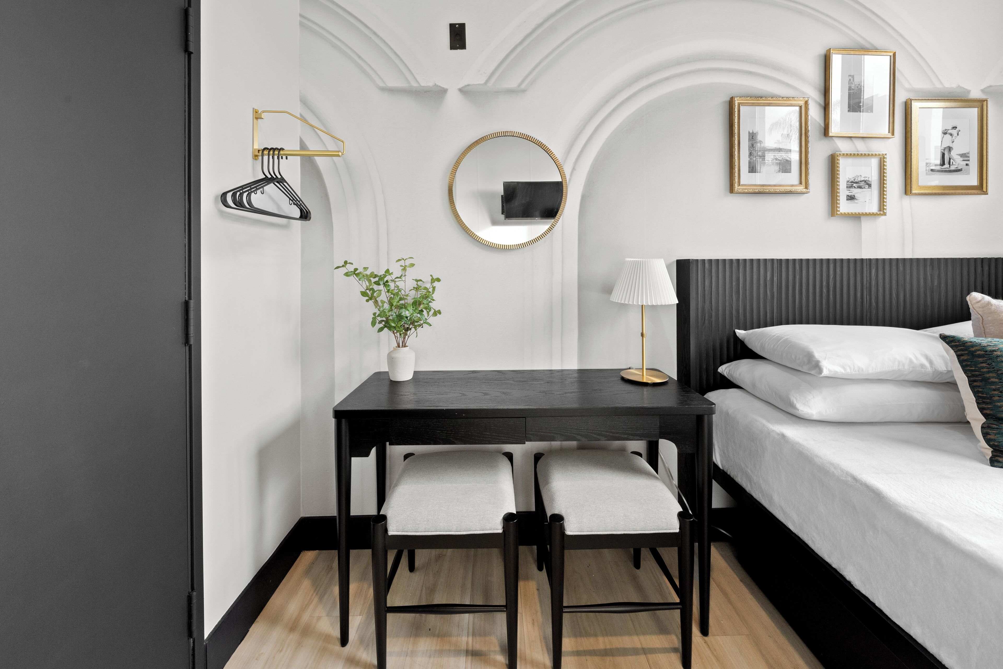 A modern bedroom with a bed, a desk with two chairs, a potted plant, and framed pictures on the wall.