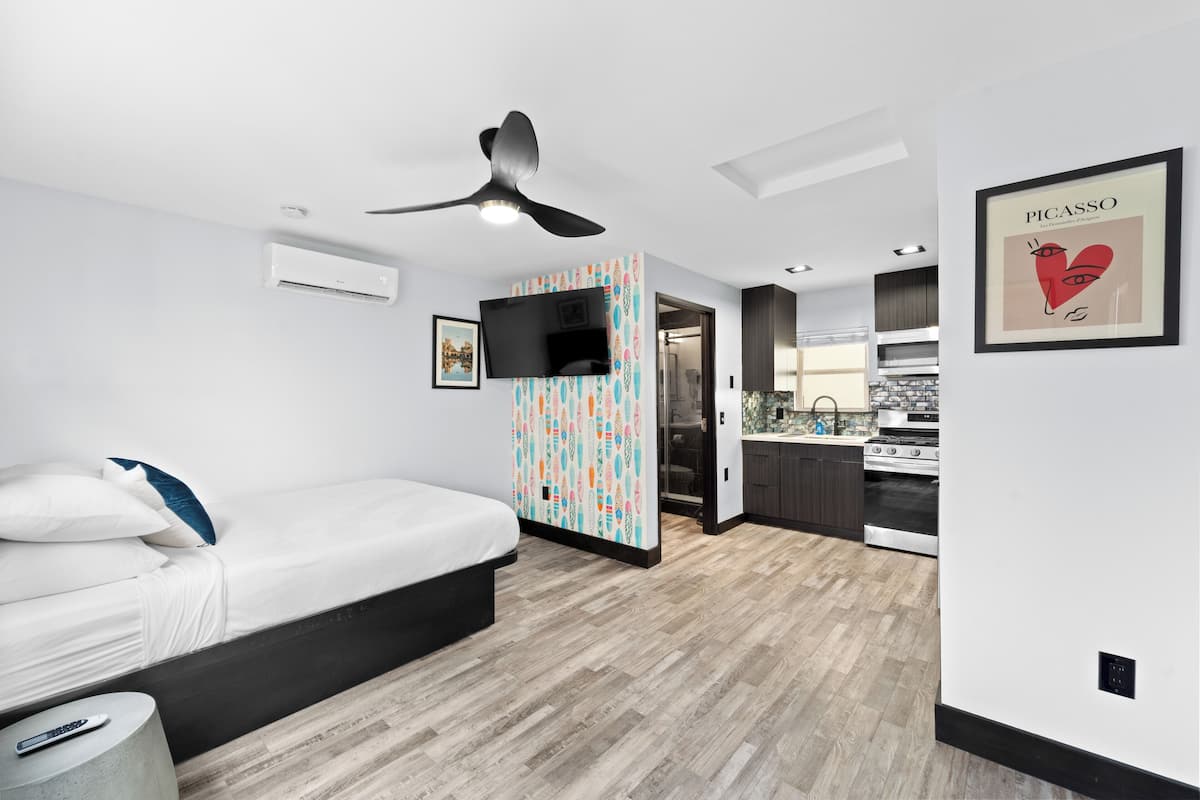Un dormitorio moderno con una cama, un televisor y una cocina al fondo.
