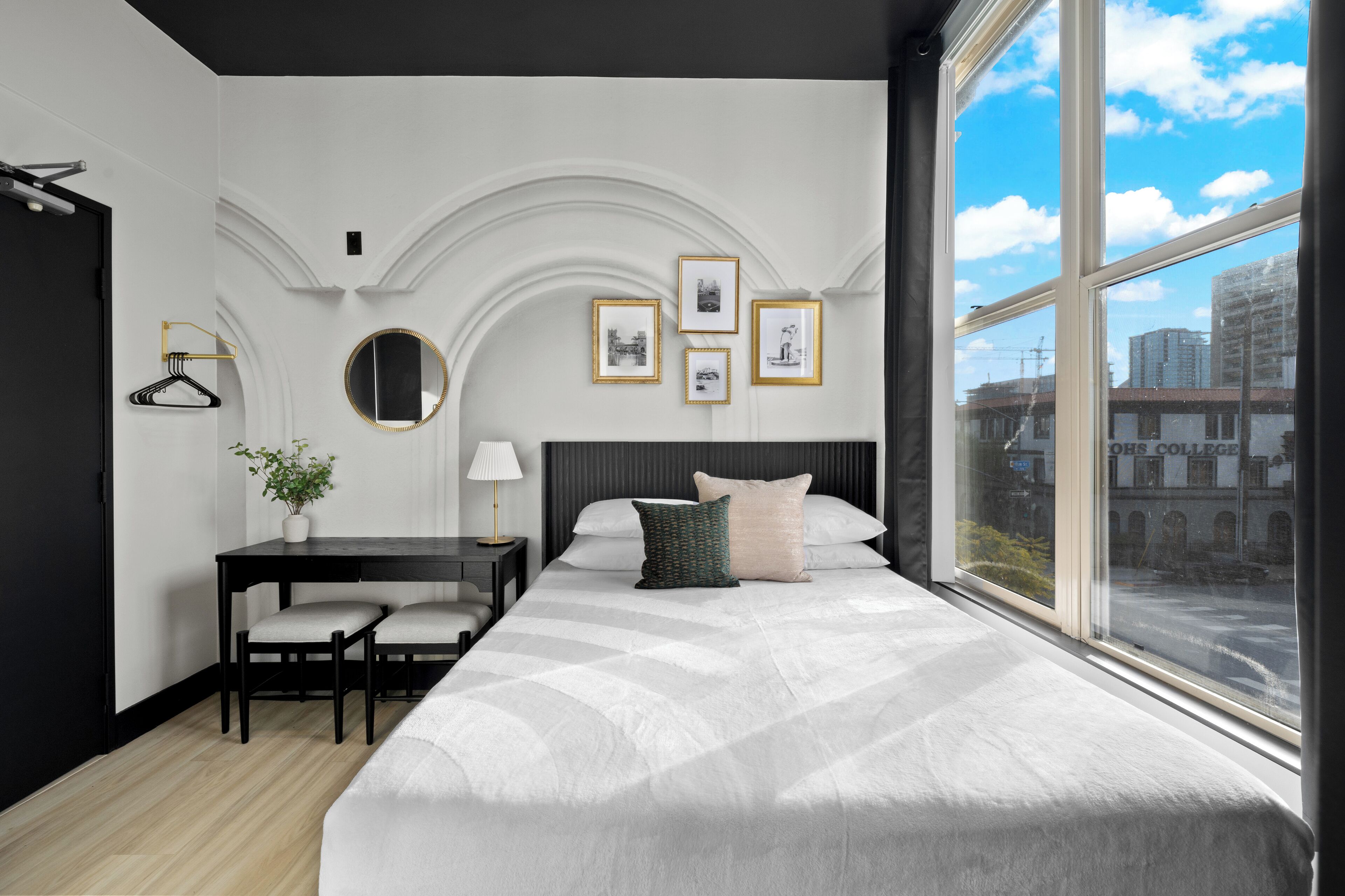 Una habitación de hotel moderna con una cama grande, un escritorio con silla, una mesita con una planta y cuadros en la pared.