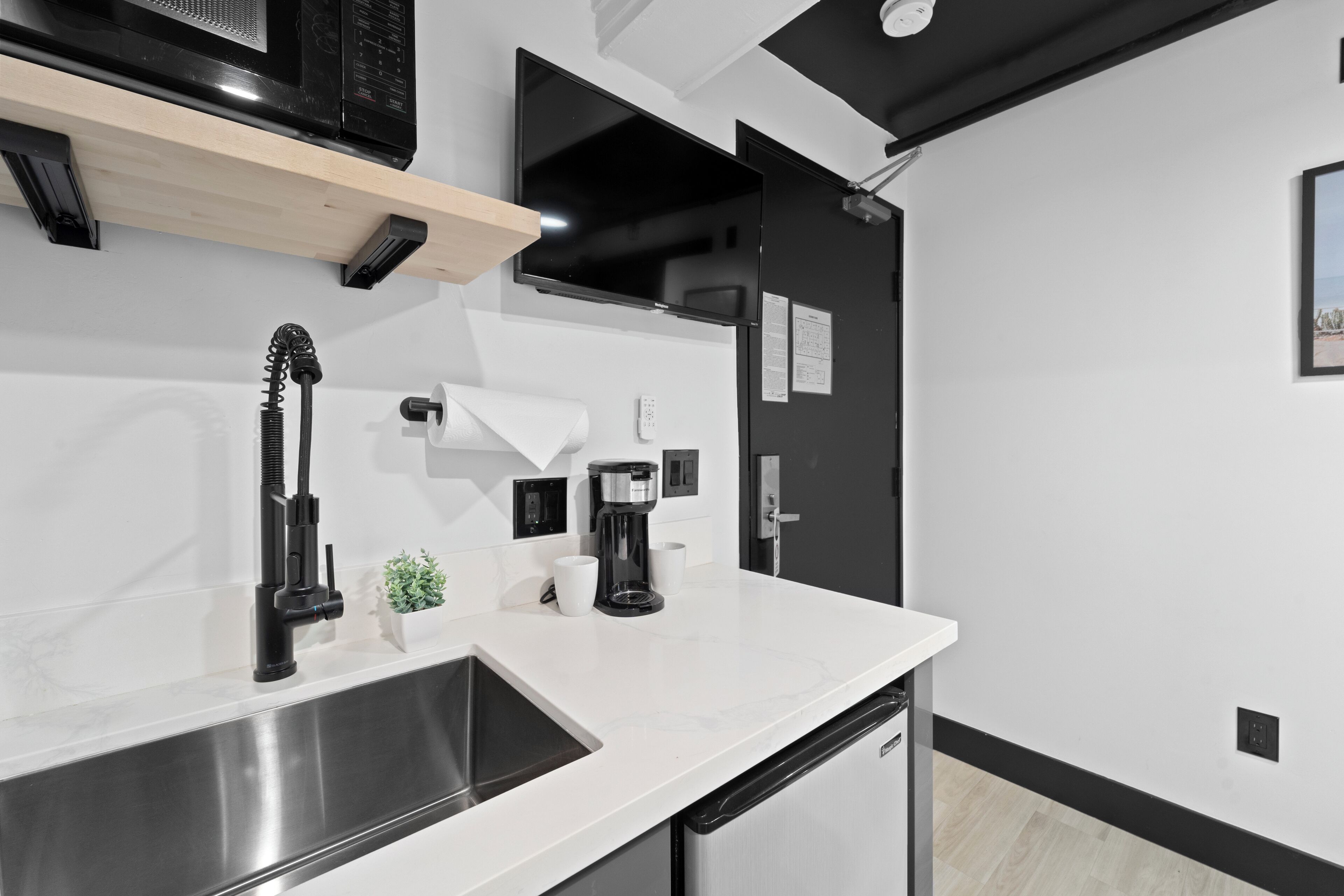 A modern kitchen with a stainless steel sink, a coffee maker, and a microwave on a wooden shelf.