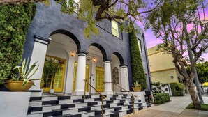 A building with a black and white tiled staircase leading to a yellow door, surrounded by greenery and columns. - The Neon Elm Hotel (San Diego)