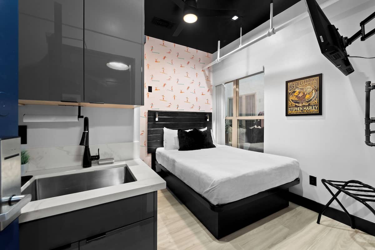 Un dormitorio moderno con cama, escritorio integrado, ventana grande y proyector montado en la pared.