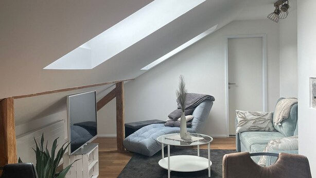 Un soggiorno in stile loft con soffitto a sbalzo, una televisione, un tavolino e posti a sedere.