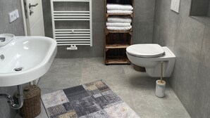 Un bagno moderno con un lavandino bianco, un water, un portasciugamani in legno e un tappeto decorato.
