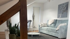 Un soggiorno moderno con pavimento in legno, un divano azzurro chiaro, un piccolo tavolino rotondo e una pianta grande.