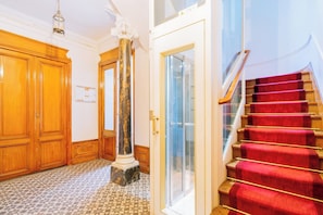 Un pasillo con puertas de madera, un columnat de mármol y una escalera con alfombra roja.