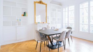 A dining room with a white table, grey chairs, a large gold-framed mirror, and a fireplace. - Charming 1-Bedroom by Champ de Mars (Paris)