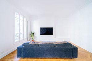 Una sala de estar minimalista con un sofá azul, una planta en maceta y una obra de arte enmarcada en la pared.