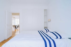 Un dormitorio con cama, una puerta que da a un comedor y una pared blanca con repisa.