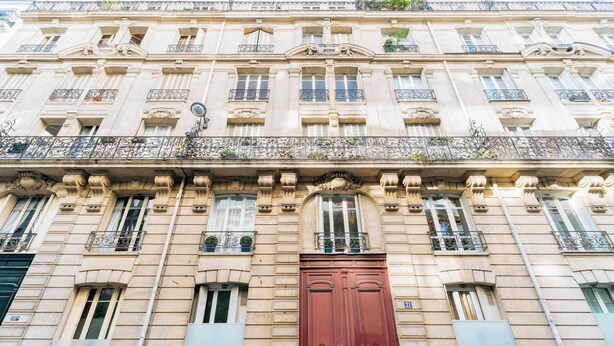 A multi-story building with ornate architectural details, including decorative moldings and a prominent red door. - Charming 1-Bedroom by Champ de Mars (Paris)