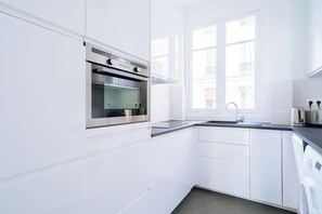 Eine moderne Küche mit weißen Schränken, einem Edelstahlbackofen, einer Spüle und einem Fenster, das für natürliches Licht sorgt.