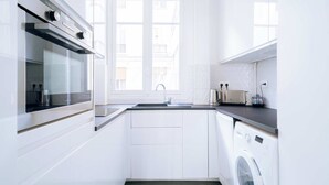 A modern kitchen with white cabinetry, a built-in oven, a washing machine, and a window providing natural light. - Charming 1-Bedroom by Champ de Mars (Paris)