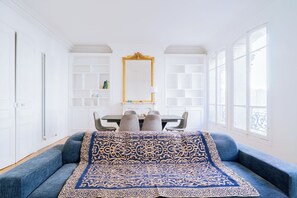 Ein Zimmer mit einer Couch, einem Esstisch mit Stühlen, einem Spiegel und einem Fenster.