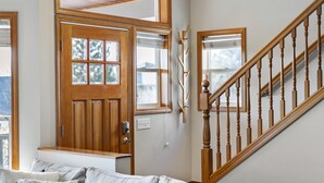 Um quarto com escada de madeira, porta com janela e um banco com almofadas.