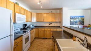 A kitchen with wooden cabinets, a microwave, a stove, a sink, and a painting on the wall. - Centrally Located Cozy Townhome in Fraser (Fraser)