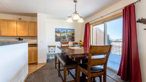 A dining area with a wooden table, benches, and a view of a mountainous landscape through a large window. - Centrally Located Cozy Townhome in Fraser (Fraser)