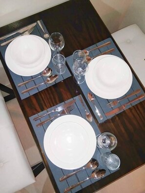Une table à manger dressée pour quatre personnes, avec de l’assiette blanche, des couverts et des verres.