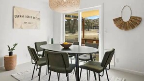 Zona pranzo con tavolo rotondo e sedie, lampadario a sospensione, specchio montato a parete e insegna con l'anno di fondazione.