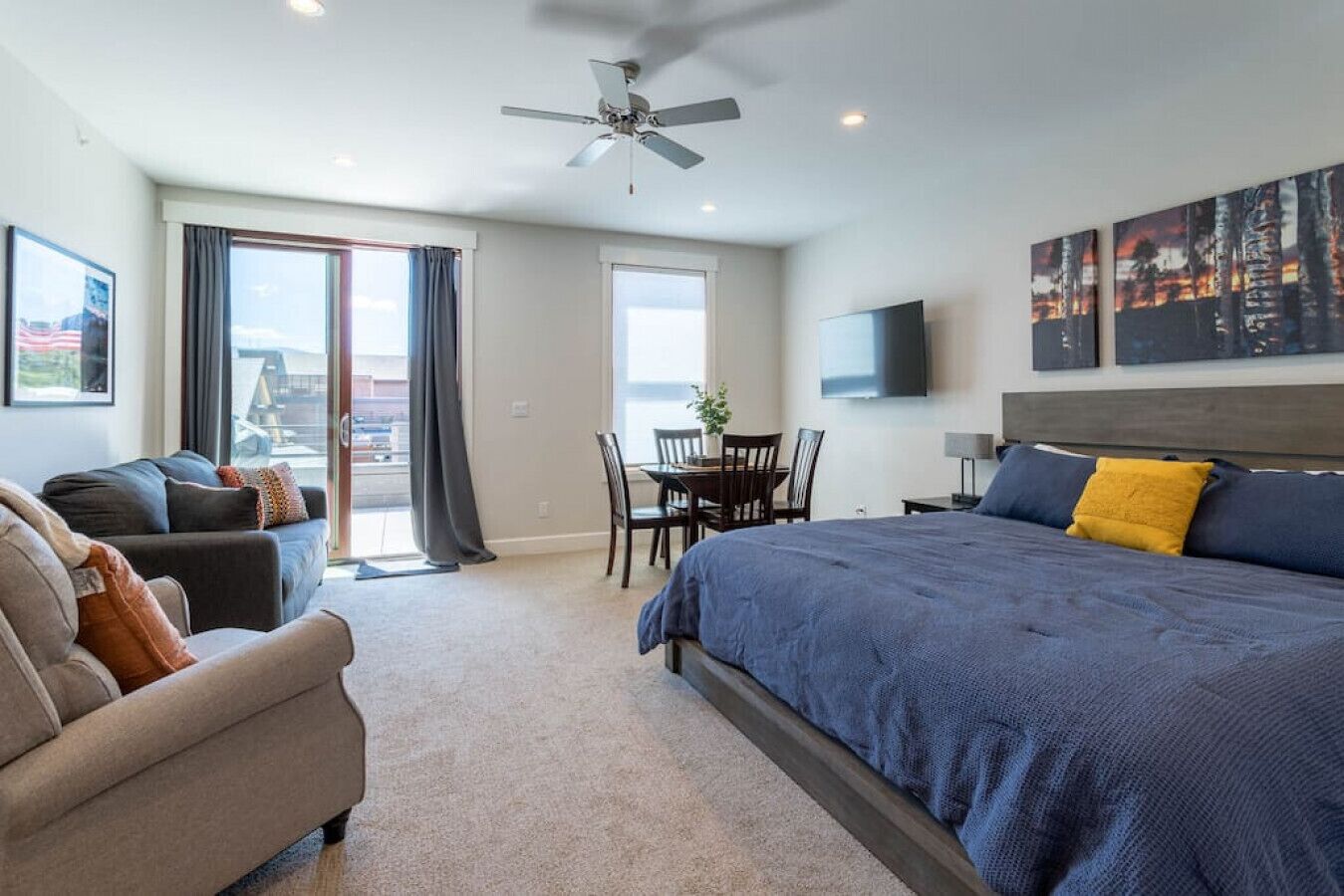 A modern hotel room with a large bed, a sofa, a dining table, and a ceiling fan.
