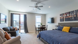 A modern hotel room with a large bed, a sofa, a dining table, and a ceiling fan. - Mad Moose Retreat: Gorgeous Condo by Grand Lake! (Grand Lake)