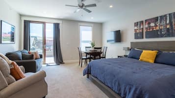 A modern hotel room with a large bed, a sofa, a dining table, and a ceiling fan.