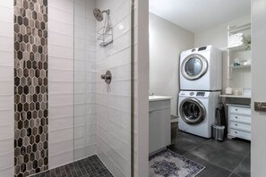 Ein modernes Badezimmer mit Dusche, einer integrierten Waschmaschine und einem kleinen Waschbecken.