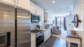 A modern kitchen with stainless steel appliances, a microwave, and a gas stove. There is a dining area with a sofa and a small table.