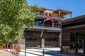 Ein modernes Gebäude mit zweigeschossiger Bauweise, großen Fenstern und einer Holz-Pergola im oberen Bereich.