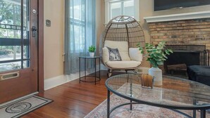 A living room with a glass coffee table, a wicker chair, a fireplace, and a large window. - Historic Bungalow w/Game Room by Downtown Tampa! (Tampa)