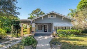 A single-story house with a covered porch, a garage, and a well-maintained front yard with potted plants. - Historic Bungalow w/Game Room by Downtown Tampa! (Tampa)