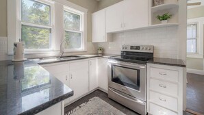 A kitchen with white cabinets, a stainless steel oven, and a window with a view of trees. - Historic Bungalow w/Game Room by Downtown Tampa! (Tampa)