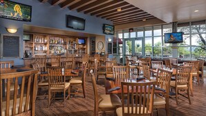 A bar area with wooden furniture, a bar counter with various bottles, and a large window offering a view of the outdoors. - Starr Pass Spring Golf Retreat - April 12-15 - 1 Bedroom Condo (Tucson)