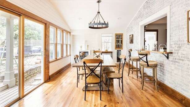 Un comedor amplio con una larga mesa de madera y sillas, una araña y ventanas grandes que ofrecen vistas al exterior.