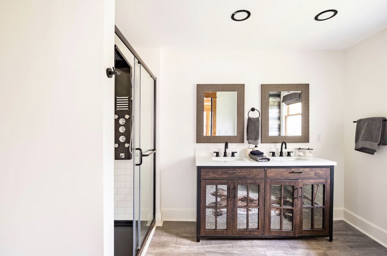 A bathroom with a double vanity, two mirrors, a shower, and a towel rack.
