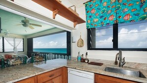 A kitchen with wooden cabinets, a white dishwasher, and a view of the ocean. - Beachfront Sunset Oasis  Adult-Only, Pool & Views (Frederiksted)