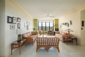 A spacious living room with a high ceiling, large windows, and a ceiling fan.