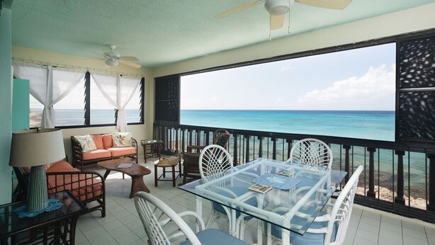 A room with a glass table, white wicker chairs, a sofa, and a ceiling fan. - Beachfront Sunset Oasis  Adult-Only, Pool & Views (Frederiksted)