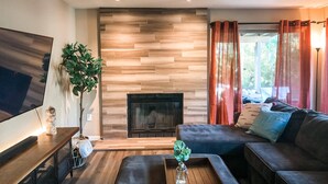 A modern living room with a fireplace, a large flat-screen TV, a sofa, and a coffee table with a vase. - Garden view home - near major higways w/high chair, pack&play, baby bathtub ways (Phoenix)