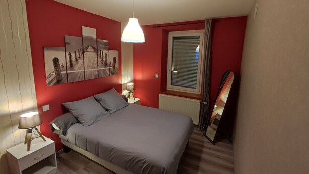 Un dormitorio con cama, mesita de noche, lámpara, ventana con persianas y espejo en la pared.